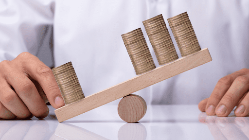 – PU Prime | More Than Trading Businessperson's Hand Showing Unbalance Between Stacked Coins On Wooden Seesaw