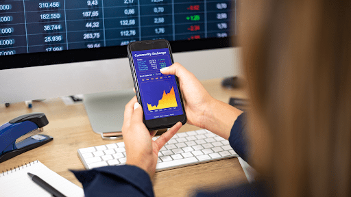 – PU Prime | More Than Trading cfd trader at desk watches oil and gas prices on her cell phone. Strong rising oil chart on the screen