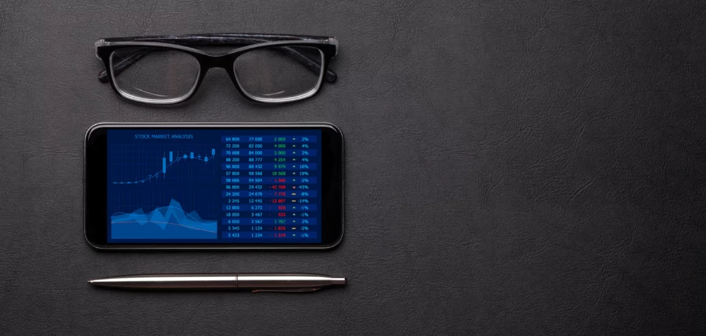 office-workspace-table-with-glasses-pen-and-mobile-phone – PU Prime | More Than Trading office workspace table with glasses pen and mobile phone showing a copy trading platform interface